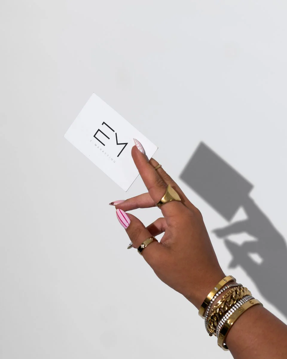 Hand holding up a card printed with the E-Marketing Agency mark, casting a shadow