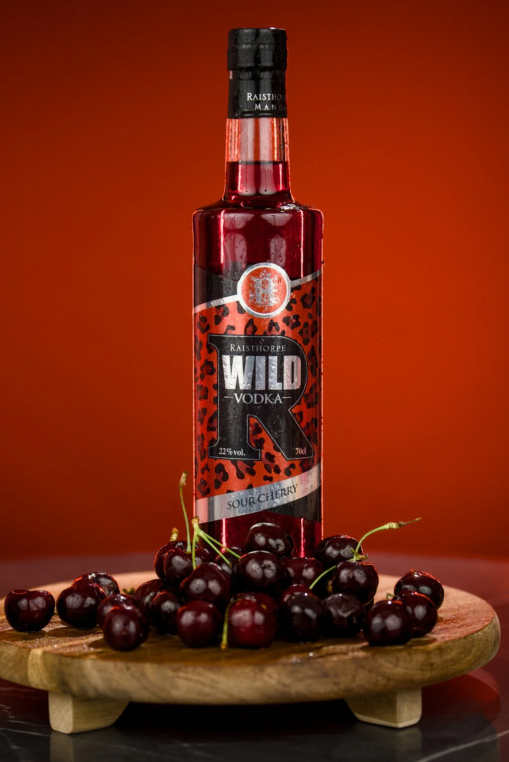 Bottle of vodka on a board of cherries against a deep orange background